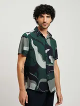 Camisa de manga corta con cuello clásico y cierre abotonado. Presenta un estampado abstracto en tonos verde, gris y negro.