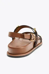Sandalia plana color marrón con doble tira delantera con detalle de hebilla, punta redonda y pulsera al tobillo con cierre de hebilla.