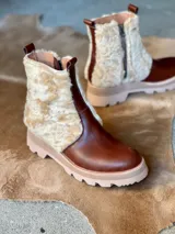 Botas cortas de cuero marrón con forro interior y exterior de corderito color crema. Tienen suela track gruesa bicolor (marrón claro y beige) y cierre lateral con cremallera.