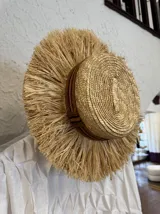 Sombrero de paja con ala ancha y adorno de flecos de paja alrededor de la copa.