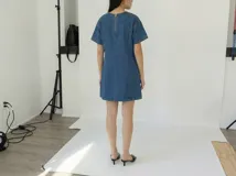 Vestido corto de jean azul con corte recto, mangas cortas y cuello redondo. Incluye cinturón plateado de cadena.