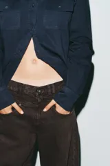 Jeans de mezclilla color marrón oscuro, tiro bajo, corte baggy barrel (ancho y holgado con caída recta). Presenta cinco bolsillos y cierre frontal con cremallera y botón metálico.