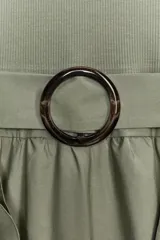 Vestido midi color verde oliva, de cuello redondo y sin mangas. Presenta un cinturón con hebilla metálica y detalle de volantes en la falda.