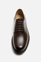 Zapato de vestir tipo derby, color marrón oscuro, con cordones, capellada de cuero brillante, forro y plantilla de cuero y suela plana.