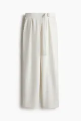 Pantalón sastrero de punto color blanco, de tiro alto con elástico oculto en la cintura y cierre decorativo. Cinturón cosido con anillas en D de metal en un lateral. Piernas ajustadas con pinzas para estilizar la silueta.