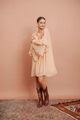 Vestido corto color salmón claro, de mangas largas acampanadas con volados y cuello redondo con volados.