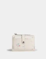 Billetera pequeña de cuerina color crema con estampado de flores y lazos. Tiene cierre superior y broche con botón para cerrar.
