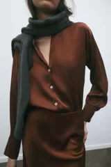 Camisa color marrón satinado, de corte holgado, con cuello solapa, escote en pico, manga larga y cierre frontal con botones.