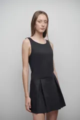 Vestido negro sin mangas, con escote redondo y falda corta plisada.