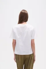 Remera blanca de manga corta y cuello redondo, con un bordado floral en tonos azules en la zona superior izquierda del pecho.