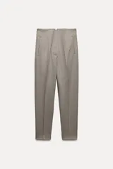 Pantalón tobillero color gris claro, de tiro alto, con bolsillos delanteros de vivo y cierre frontal con cremallera, botón interior y gancho metálico.