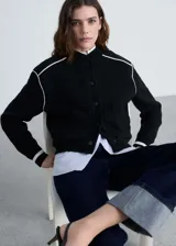 Chaqueta negra de punto con corte bomber, cierre frontal con botones a presión, bolsillos laterales y ribete blanco en cuello, puños, ruedo y hombros.
