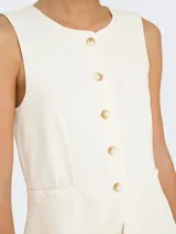 Chaleco corto color blanco hueso con cuello abierto y cierre frontal con botones. Confeccionado en tejido de punto con mezcla de poliéster y elastano. Diseño sin mangas con textura suave y calce ajustado.