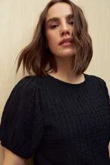 Top negro de tejido texturizado con mangas cortas abullonadas y cuello redondo.
