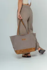 Bolso tipo tote color gris con base de cuero marrón y asas de cuero marrón.