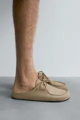 Zueco color beige de piel con acabado serraje, detalle de cordones y bordón en el empeine, plantilla acolchada, horma redonda y suela ultrafina a contraste.