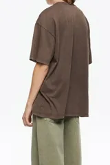 Camiseta de algodón orgánico color beige, corte oversize y manga corta ancha. Presenta un estampado central enmarcado con motivos florales y el texto "BIMBA Y LOLA" en la parte superior e inferior del diseño.