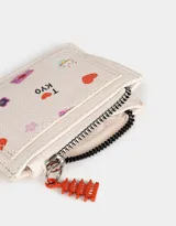 Monedero de cuerina color crudo con cierre superior, bolsillo frontal estampado con motivos japoneses y dije colgante de pagoda roja.