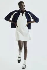 Vestido corto blanco de piqué con cuello polo, tapeta de botones y falda acampanada.