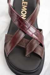 Sandalia marrón con tiras cruzadas de cuero con textura de cocodrilo, suela track color negro y hebilla metálica.