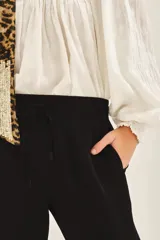 Pantalón babucha color mostaza, con elástico en la cintura y cordón ajustable con terminaciones metálicas. Tiene bolsillos diagonales en el frente y falsos bolsillos ojal en la espalda.