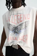 Musculosa blanca con efecto lavado, cuello redondo y sisa ancha. Estampado frontal con la leyenda "L.A. Legend Trailblazer" y un águila.