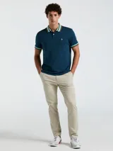 Chomba azul petróleo de manga corta con cuello polo y puños acanalados a rayas en celeste, naranja y blanco. Logo bordado en el pecho. Cierre con dos botones.