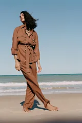 Camisa color marrón con cuello solapa y manga larga acabada en vuelta con trabilla y botón. Bolsillos delanteros de plastrón con solapa. Bajo con aberturas laterales. Cierre frontal con botones y cinturón de la misma tela.