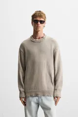 Jersey de punto color beige, de corte holgado, con cuello redondo y manga larga. Tiene efecto lavado y rotos en toda la prenda.