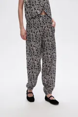Pantalón slouchy de viscosa con estampado floral en tonos beige y negro, bolsillos laterales, cintura alta y detalle de punto smock en los tobillos.