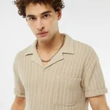 Camisa beige de manga corta con tejido calado, cuello clásico y cierre frontal con botones.