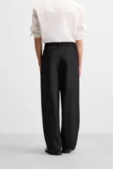 Pantalón negro de corte ancho con cinturón de tela con hebilla metálica y pliegues frontales.