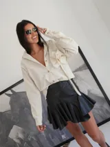 Camisa color crema con bordado de flores y roseta decorativa en el frente. Tiene botones de cuerno, corte holgado y espalda más larga.