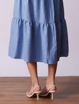 Vestido midi celeste de tencel con cuello a la base y escote en V. Cintura con frunces y lazo de ajuste. Terminación de ruedo con volado.