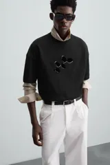 Camiseta negra de corte holgado, cuello redondo y manga corta. Estampado frontal con diseño abstracto en color blanco.