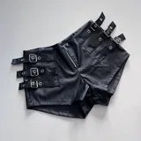 Short de cuero negro con tiras y detalles metálicos, de corte ajustado.