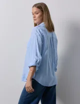 Camisa celeste de lino, con cuello con solapa, escote en V y abertura central con botones. Largo de manga regulable con presilla y botón. Delantera con bolsillo aplicado.