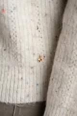 Sweater de tejido de punto color blanco roto, con motas de colores (efecto tweed o confetti), cuello alto con cierre metálico parcial y calce oversize.