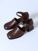 Zapato de cuero negro con textura de cocodrilo, con correa al tobillo y tacón geométrico.