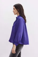 Camisa blanca de manga larga confeccionada en viscosa con acabado sandwash, de textura suave y aterciopelada. Cuello camisero con botón en forma de corazón y frunces en el canesú delantero y la espalda.