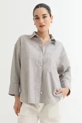 Camisa color beige de corte amplio, con cuello clásico, manga larga y bolsillo en el pecho.