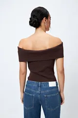 Top tejido color blanco con escote bardot que deja los hombros al descubierto y punto acanalado.