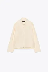 Cazadora tipo bomber color crema confeccionada en hilatura con mezcla de algodón. Cuello solapa y manga larga. Bolsillos delanteros. Forro interior a tono. Bajo ajustable. Cierre frontal con cremallera metálica.