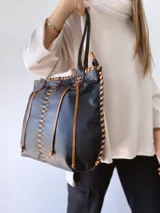 Bolso tipo tote de cuero negro con costuras a la vista en color camel. Tiene doble asa de hombro y está forrada en tela.