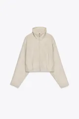 Cazadora corta color beige de cuello alto y manga larga. Tiene bolsillos laterales y cierre frontal con cremallera metálica.