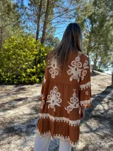 Vestido corto color marrón con estampado floral blanco, cuello mao y mangas 3/4 acampanadas.