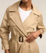 Trench coat largo color beige confeccionado en gabardina de algodón, con cuello solapa, cierre frontal abotonado, cinturón con hebilla, bolsillos laterales y trabillas en los puños.