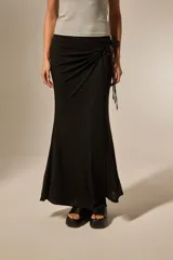 Falda larga negra con detalle de nudo lateral y tiras colgantes, de corte ajustado en la parte superior y ligeramente acampanado en el ruedo.