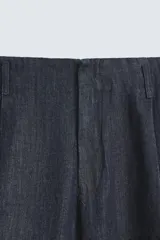Pantalón de denim azul oscuro, corte wide fit, largo cropped, con pliegues frontales, bolsillos laterales y traseros asimétricos. Cierre frontal con cremallera y gancho metálico oculto.
