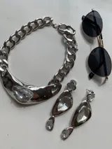 Collar metálico plateado estilo chunky con cadena de eslabones gruesos y dije central con forma de medialuna irregular con incrustación de cristal transparente.